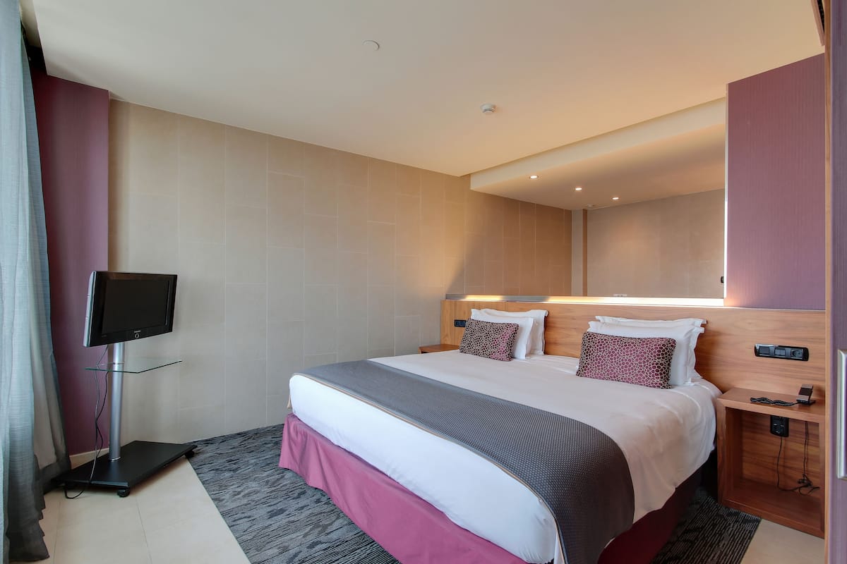 Ein Hotelzimmer mit einem Bett, einem Fernseher auf einem Tisch, einem Nachttisch und einem Spiegel.