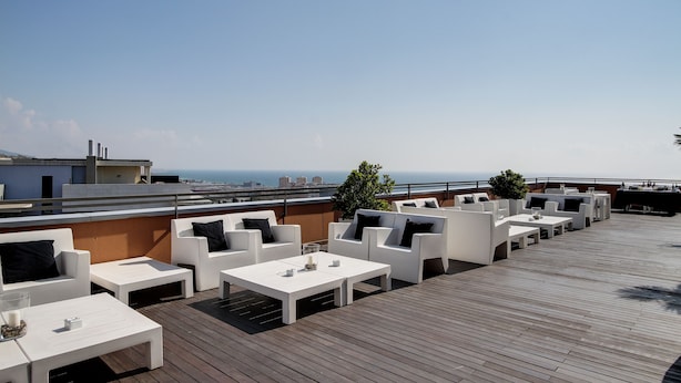 Une terrasse sur le toit, dotée de mobilier d’extérieur blanc, comprenant des canapés et des tables, et offrant une vue sur le paysage urbain.