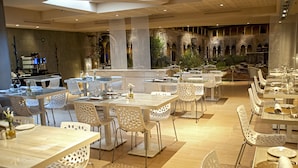 Un restaurant spacieux avec de hauts plafonds, un mobilier blanc et moderne, et une vue sur une cour extérieure.