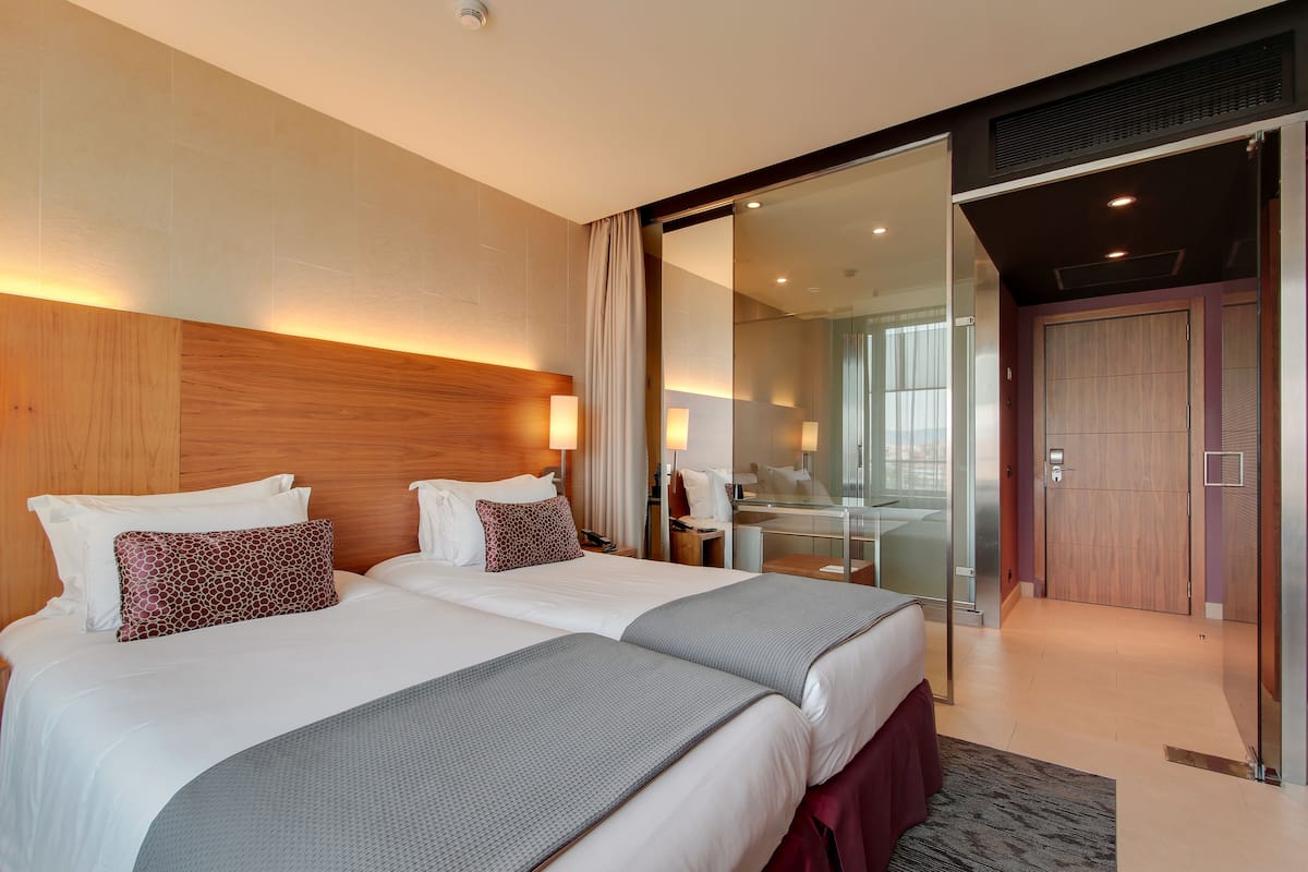 Ein Hotelzimmer mit zwei Betten, einer Glaseinrichtung, einem Holz-Kopfende und einer Schiebetür zum Badezimmer.