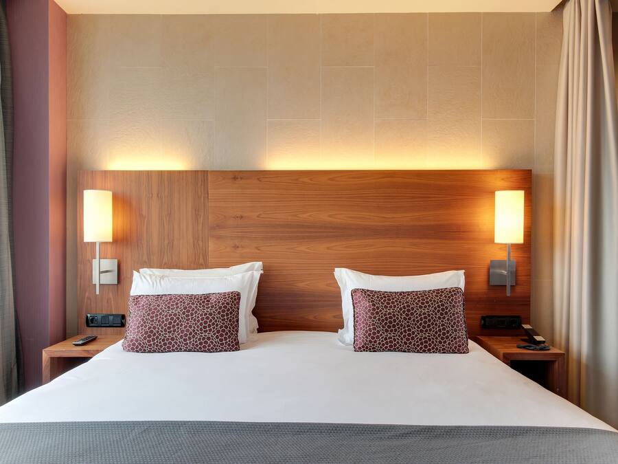 A hotel room with a large bed, two bedside tables, a wooden headboard, and wall-mounted lamps.