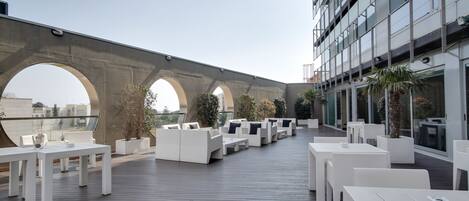 Una terraza en la azotea con mobiliario blanco, ventanas amplias y vistas de la ciudad.