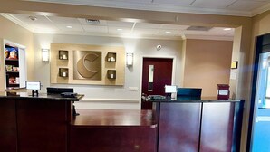 A reception area with a wooden reception desk, a wall-mounted clock, and a digital welcome sign. - Comfort Inn & Suites Fort Walton Beach - Destin West (Fort Walton Beach)
