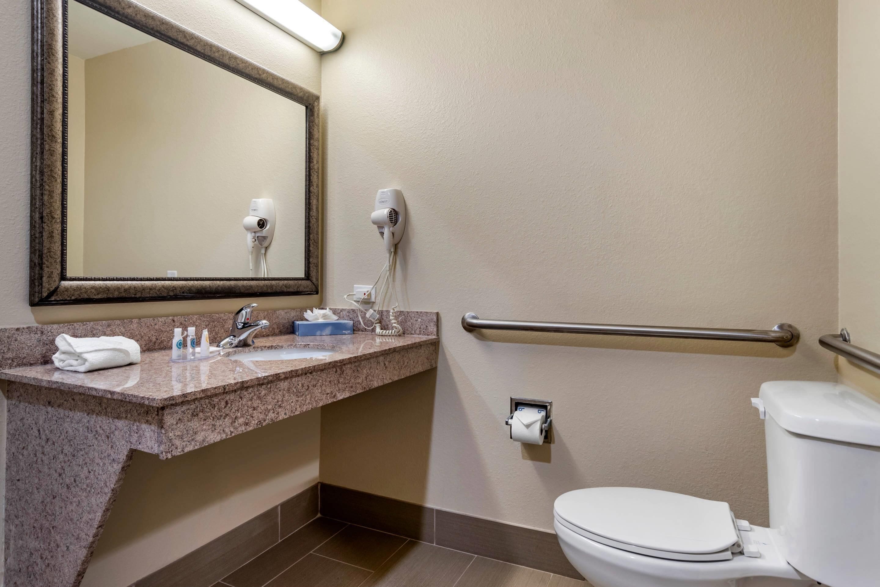 A bathroom with a sink, mirror, towel, hair dryer, and toilet.