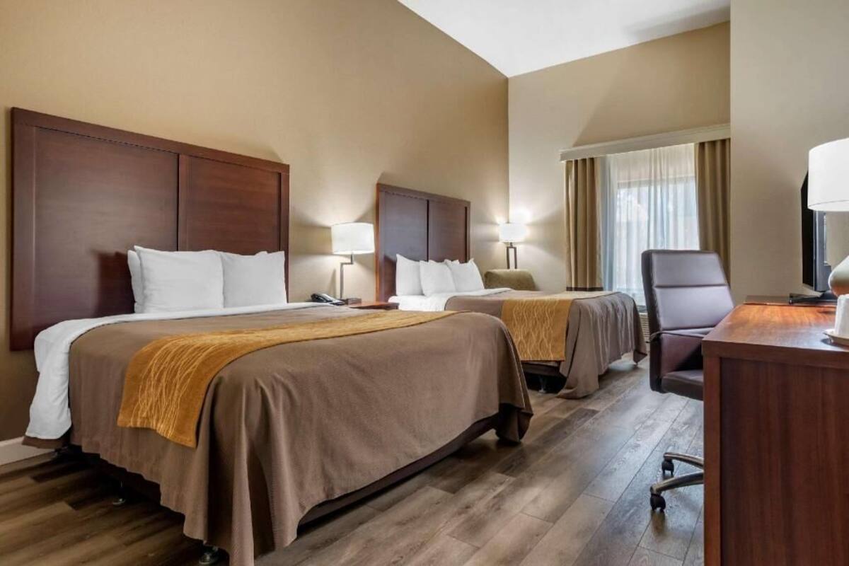 A hotel room with two beds, a desk, and a chair.
