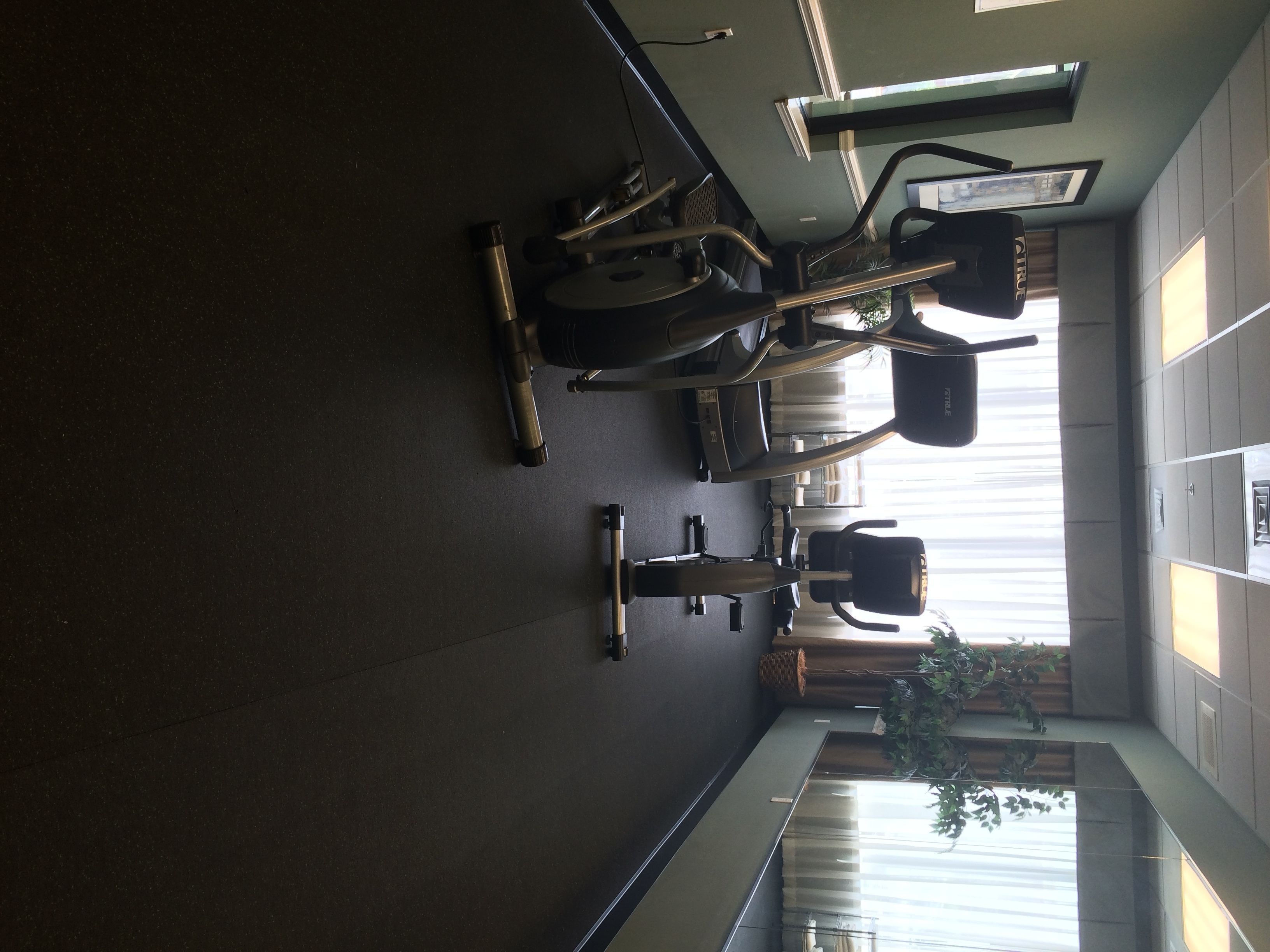 Une salle de sport équipée de machines de cardio, d’un banc de musculation et d’un miroir.