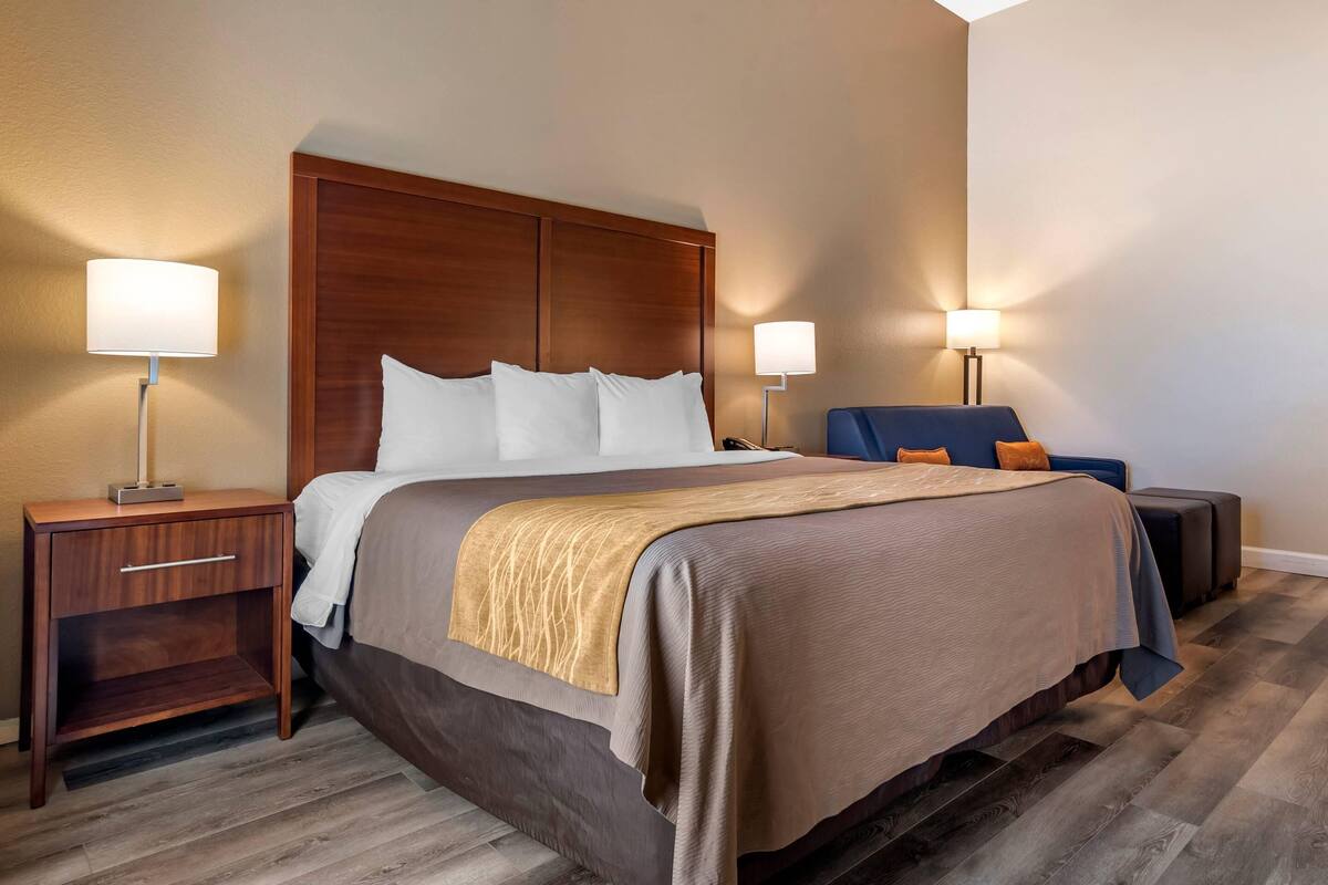A hotel room with a large bed, two bedside tables, a nightstand, a chair, and two floor lamps.