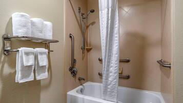 Un baño con bañera, ducha con barras de apoyo y toallero con varias toallas.