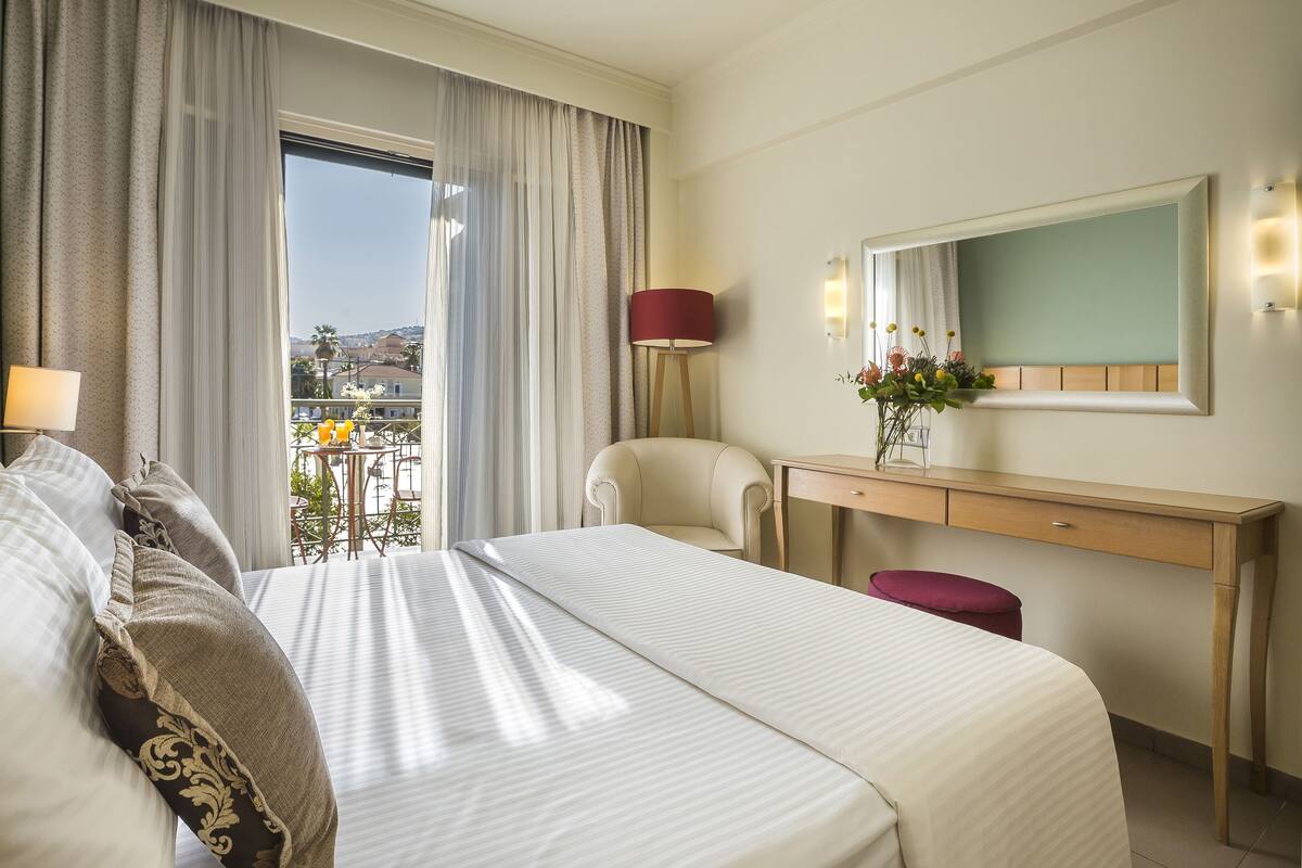 Habitació d'hotel amb un llit, escriptori, cadira, taula petita amb una làmpada i vista exterior.