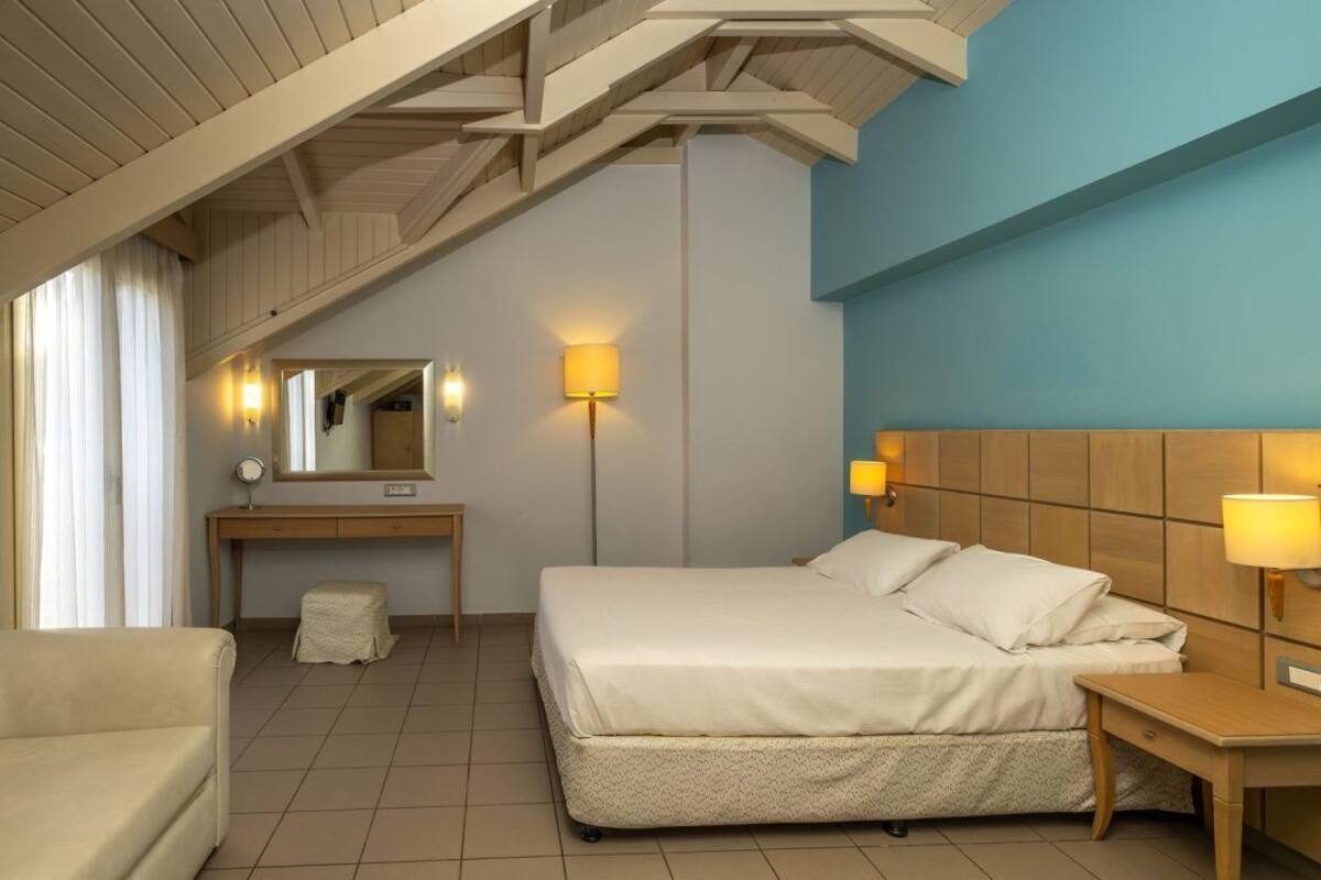 Habitació d'hotel amb llit, escriptori, cadira, mirall i dues làmpades de nit.