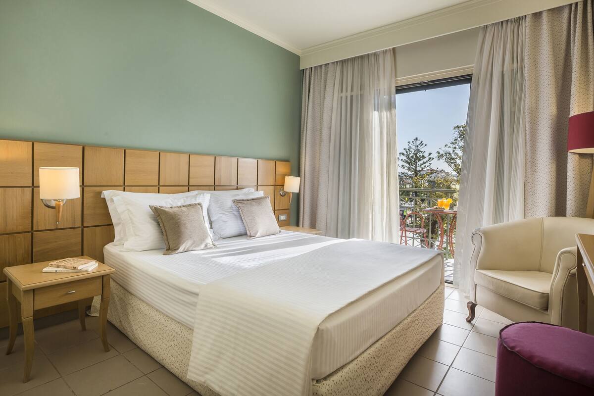 Habitació d'hotel amb un llit gran, dues taules de nit, una cadira i un balcó amb taula i cadires.