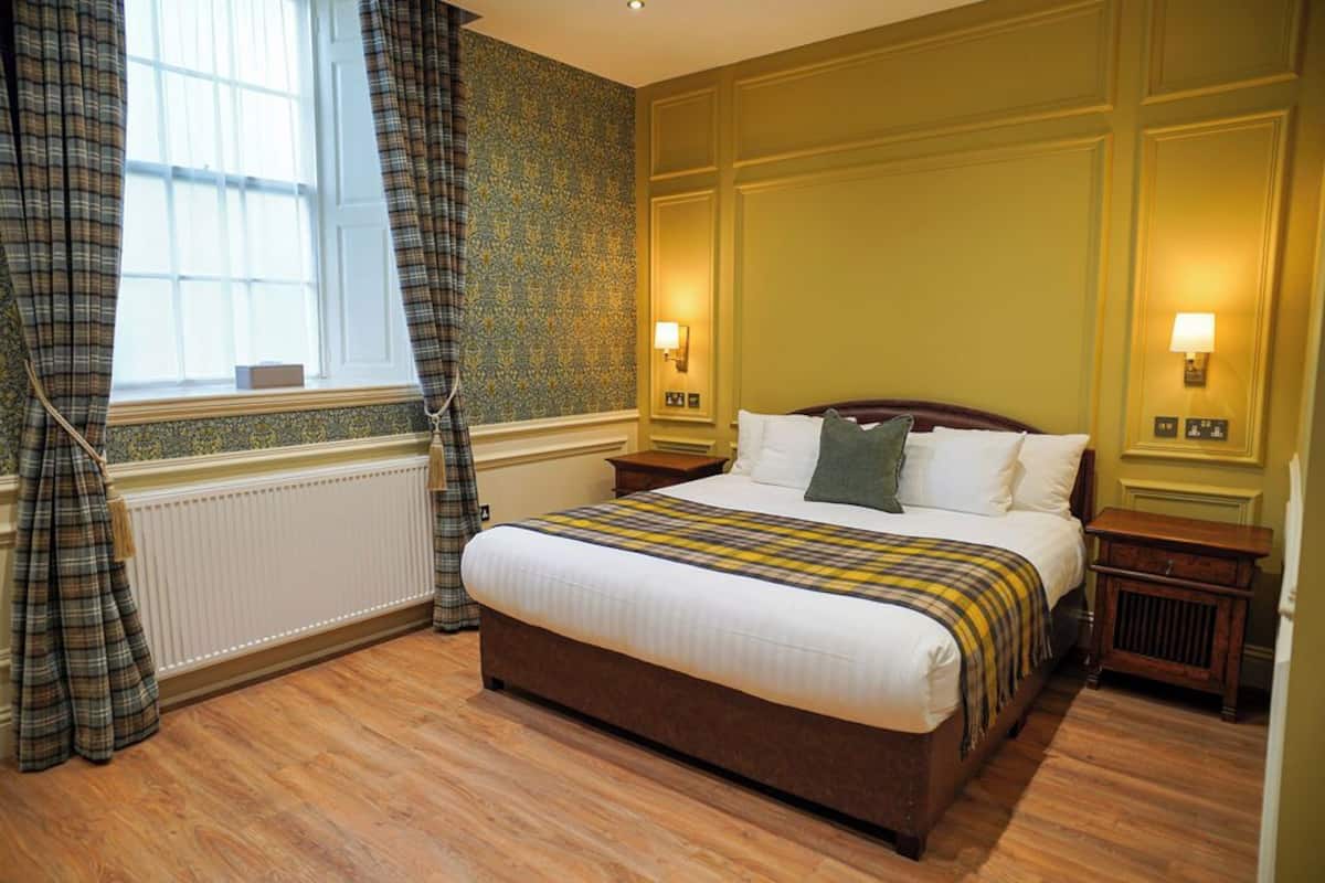 A hotel room with a large bed, two bedside tables, a window with curtains, and wall-mounted lamps.