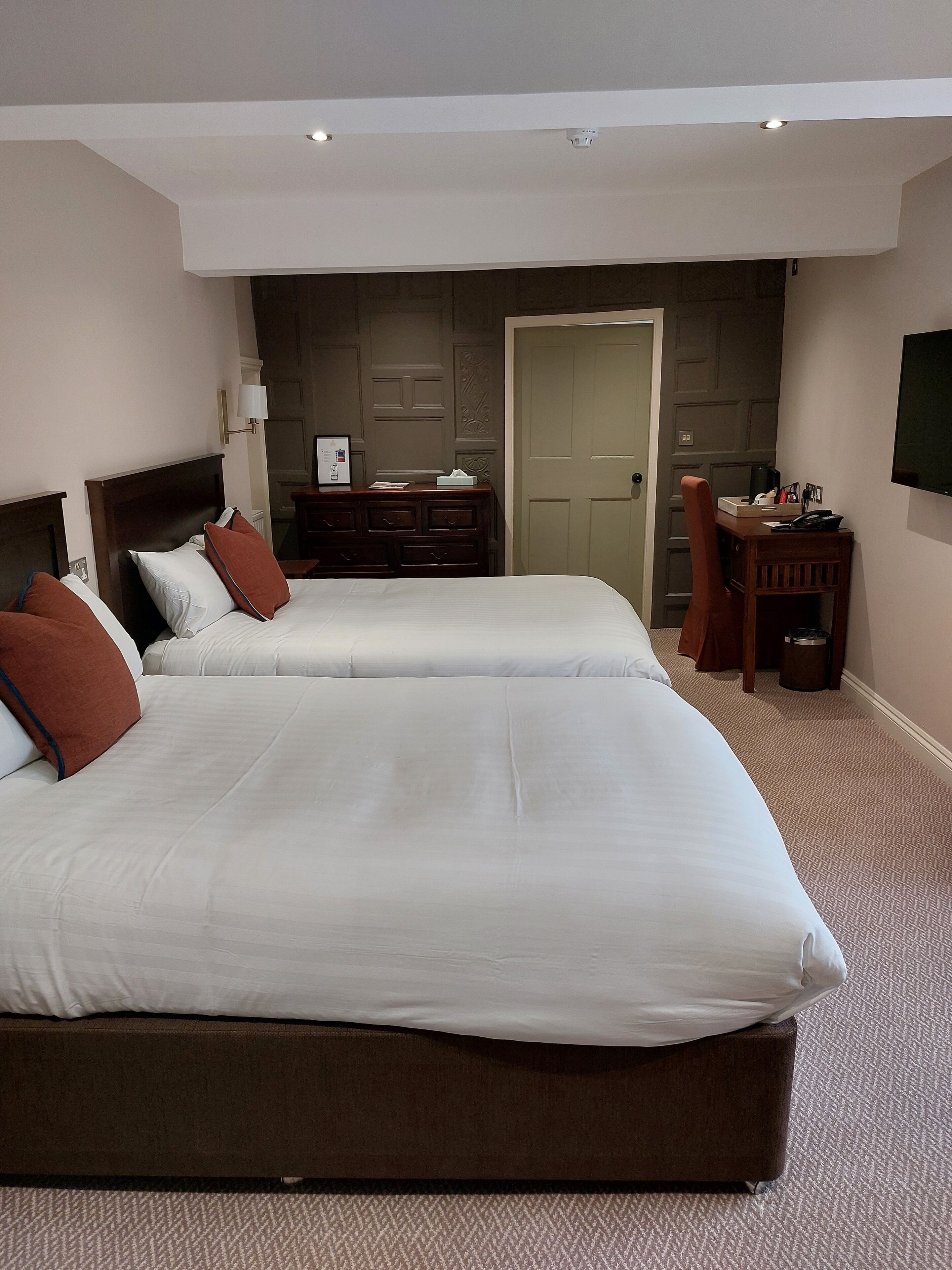 A hotel room with two beds, a dresser, a desk, and a television on the wall.