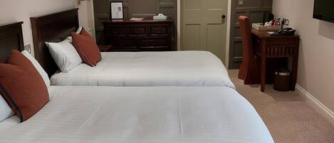 A hotel room with two beds, a dresser, a desk, and a television on the wall.