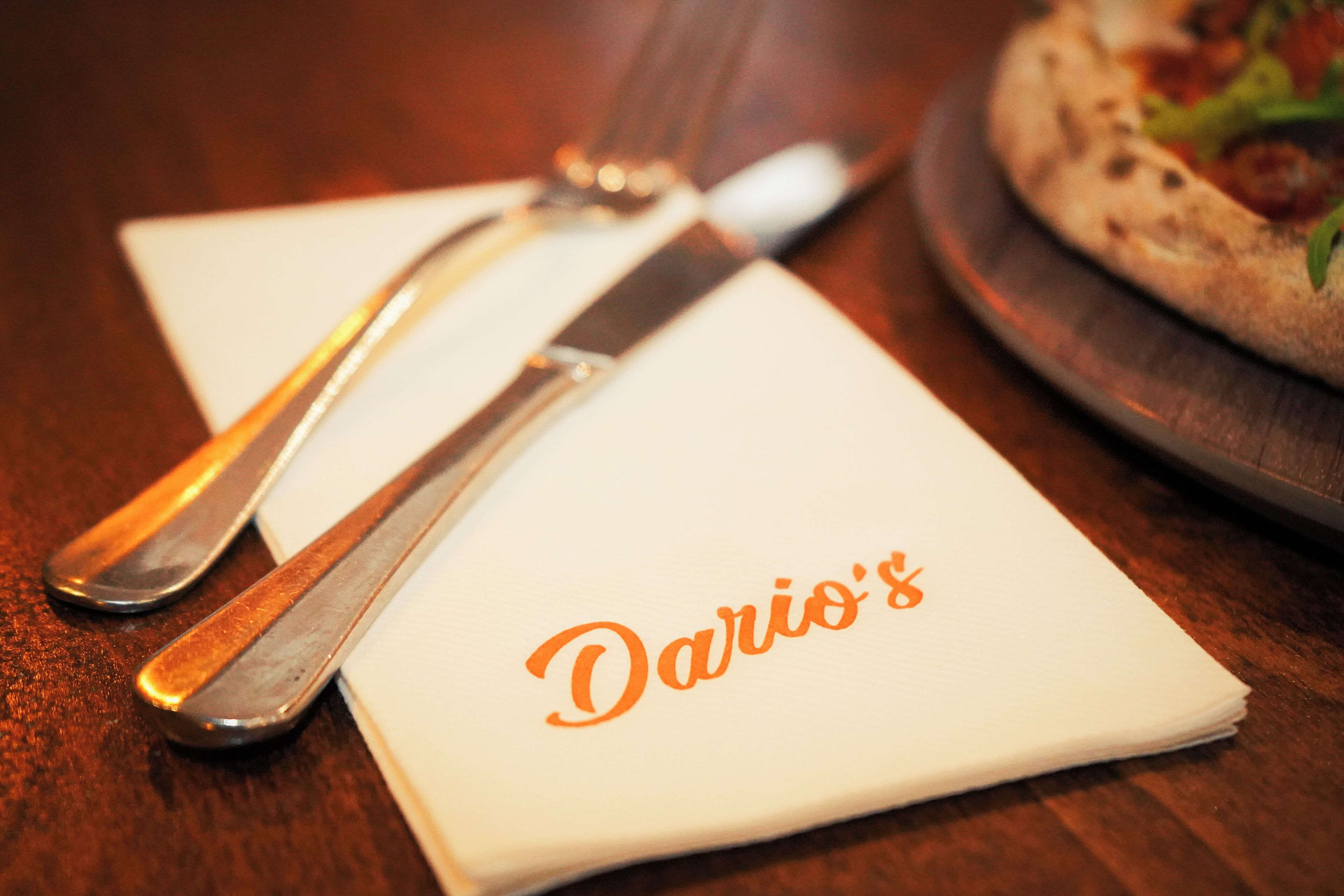A table setting with a napkin displaying "Dario's" in orange lettering, a fork, and a knife.