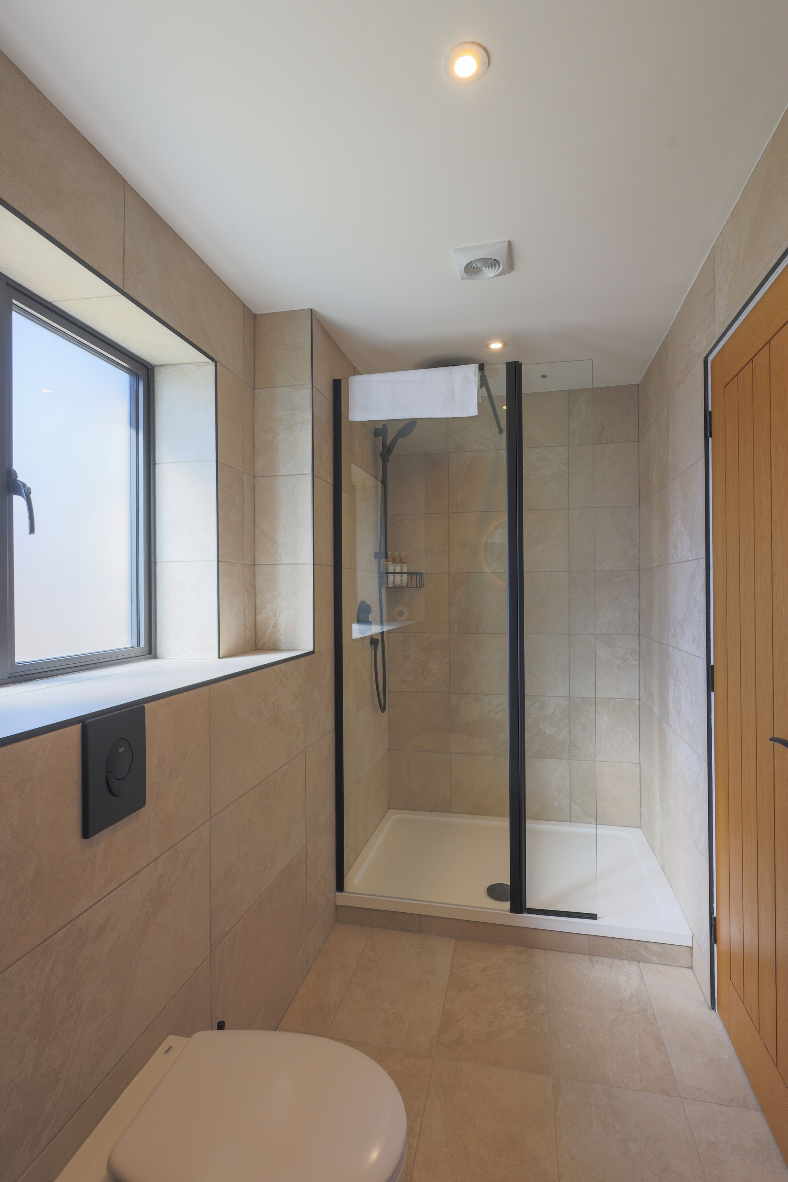 A modern bathroom with a glass-enclosed shower, a toilet, and a window providing natural light.