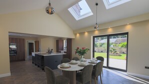 A modern kitchen with dark wood cabinets, a central island, and a dining area with a round table and chairs. There are skylights and a large sliding glass door leading to a garden. - Owston Hall Hotel (Doncaster)