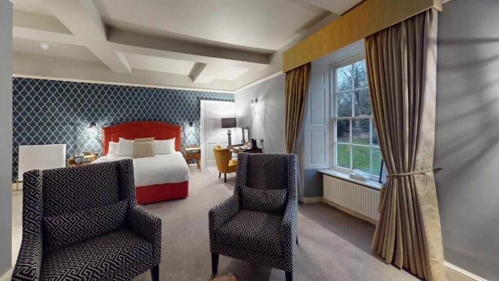 Una habitación de hotel con una cama, dos sillones, un escritorio y una ventana con cortinas.
