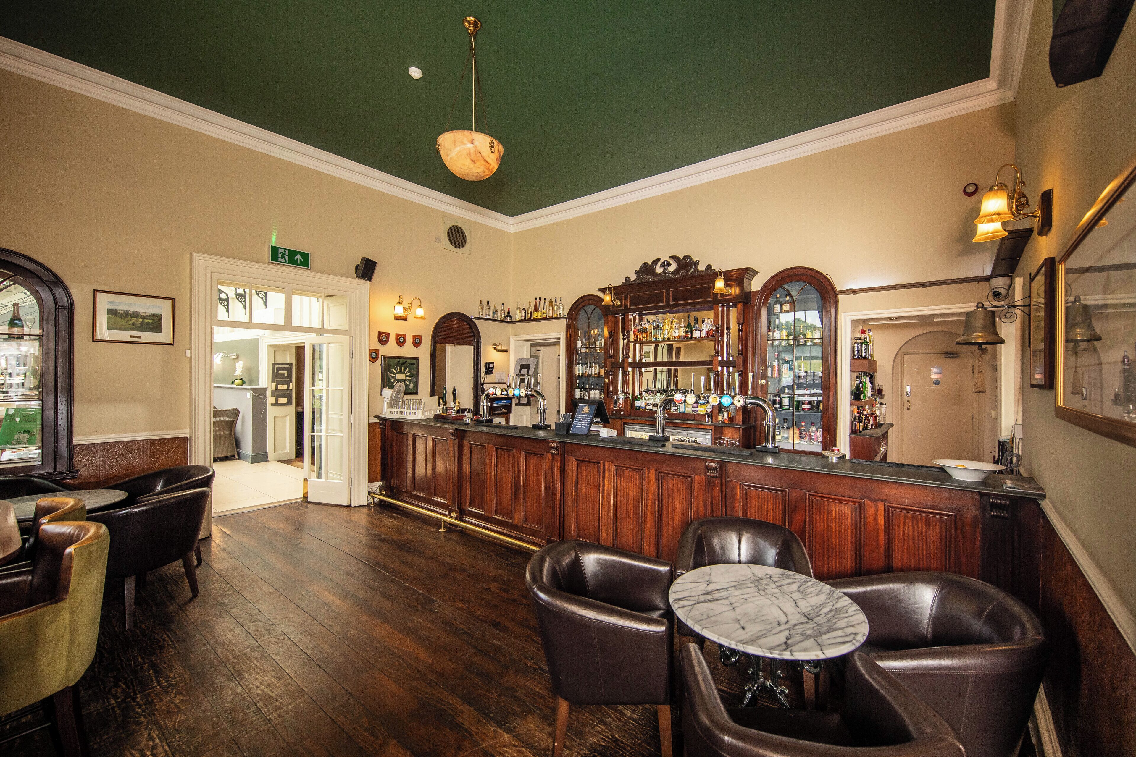 A bar area with wooden flooring, leather chairs, a marble table, and a bar counter with various bottles and a cash register.