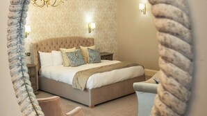 A bedroom with a tufted headboard, a bed with multiple pillows, a bedside table, and a chandelier. - Owston Hall Hotel (Doncaster)