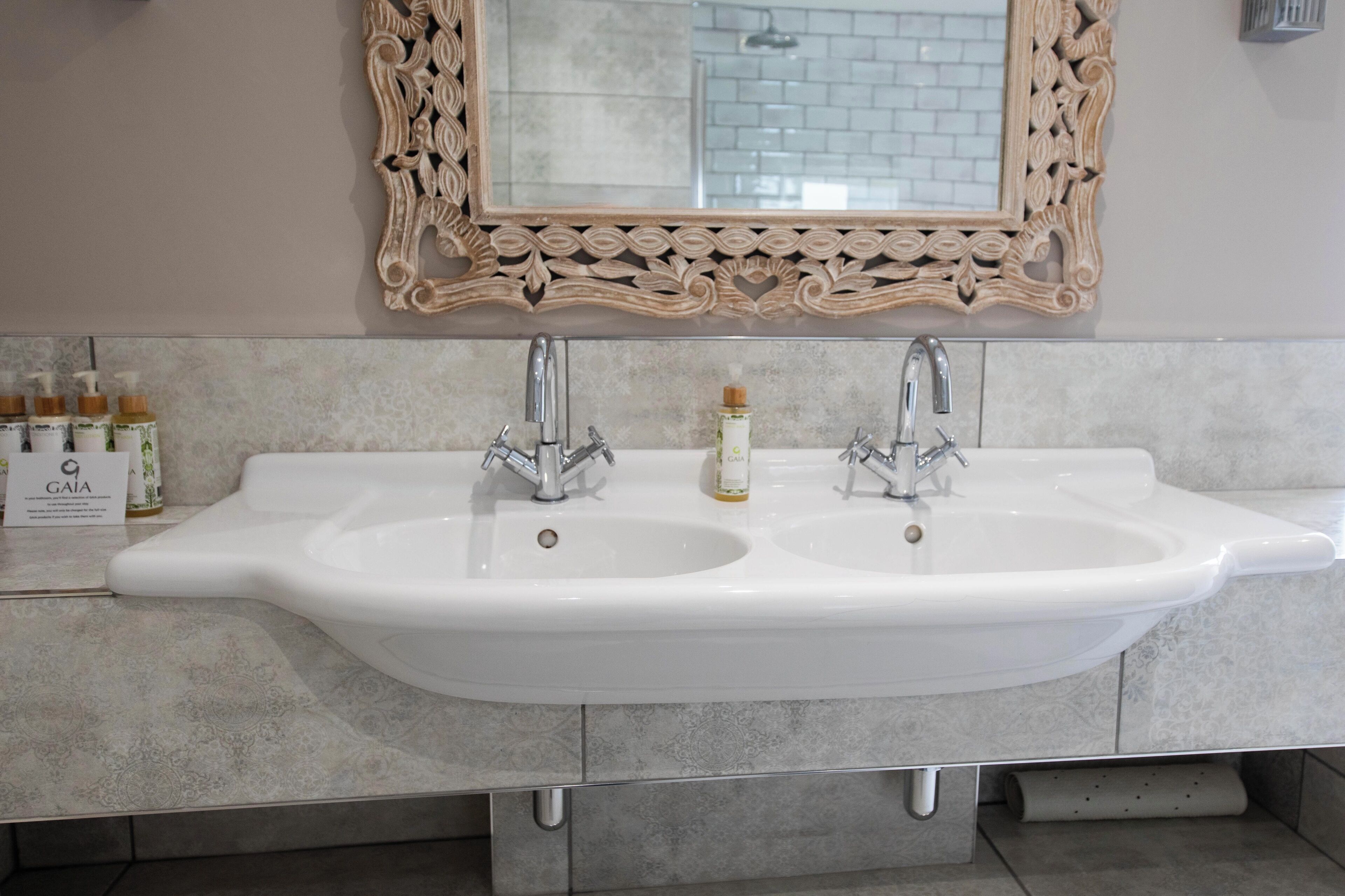 A bathroom with a double sink, two faucets, and a decorative mirror with an ornate frame.