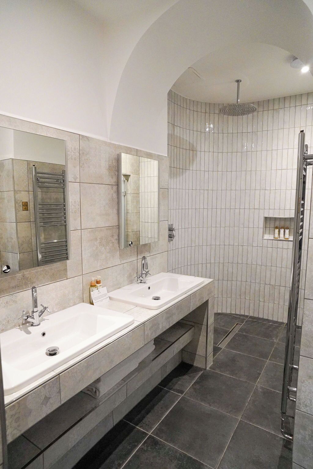 A modern bathroom with two sinks, a large mirror, and a shower area.