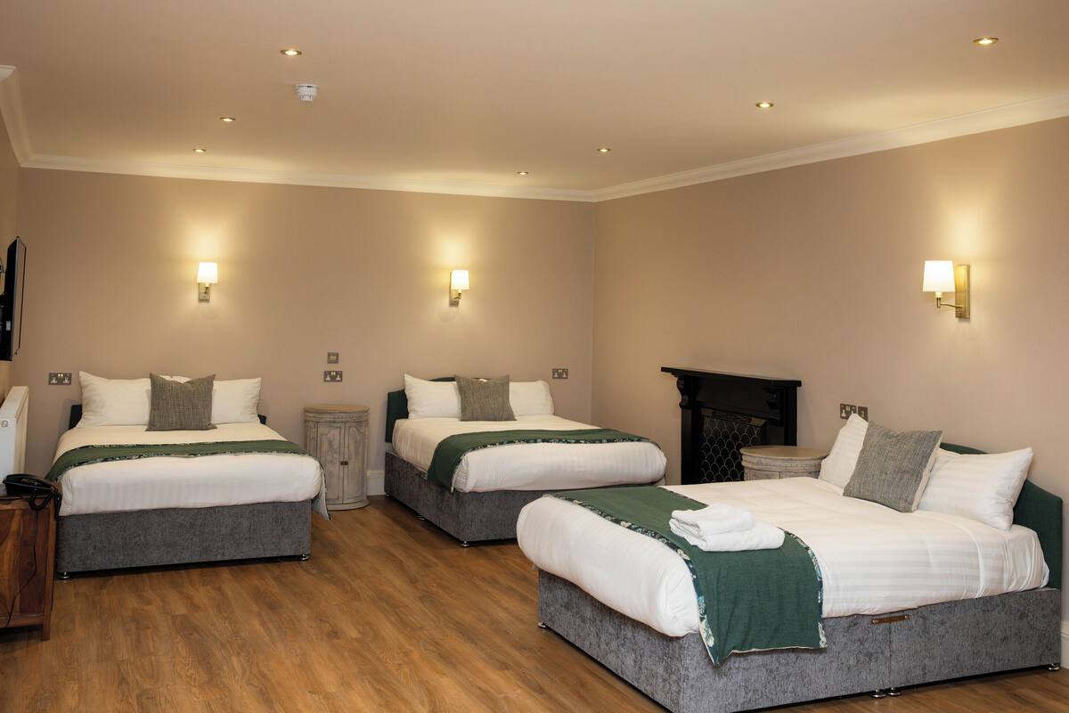 A hotel room with two beds, wooden flooring, and wall-mounted lighting.