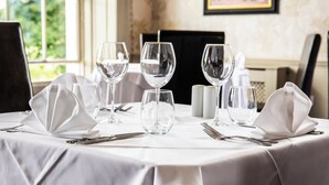 A table set for dining with wine glasses, water glasses, and cutlery, in a room with a window and a framed picture on the wall. - Owston Hall Hotel (Doncaster)