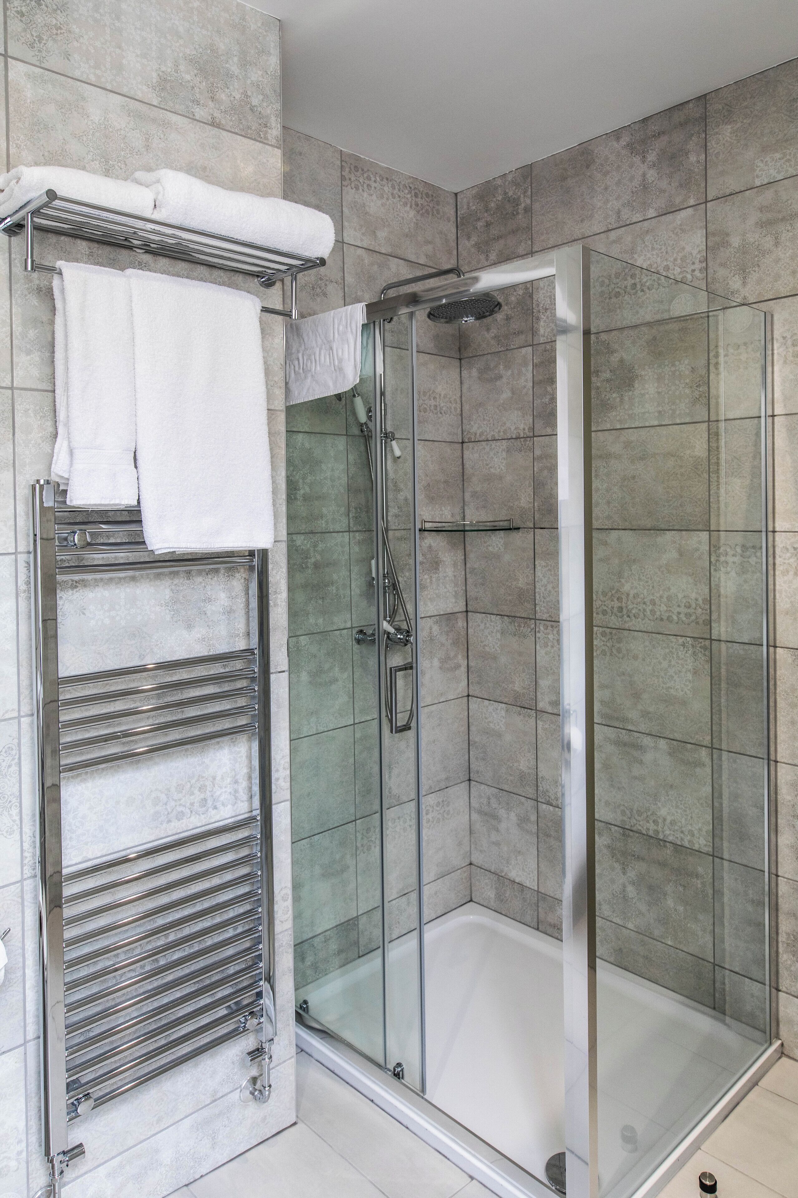 A modern bathroom with a glass-enclosed shower, a towel rack with folded towels, and a chrome towel warmer.