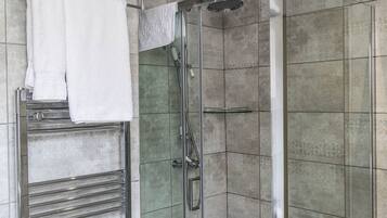 A modern bathroom with a glass-enclosed shower, a towel rack with folded towels, and a chrome towel warmer.