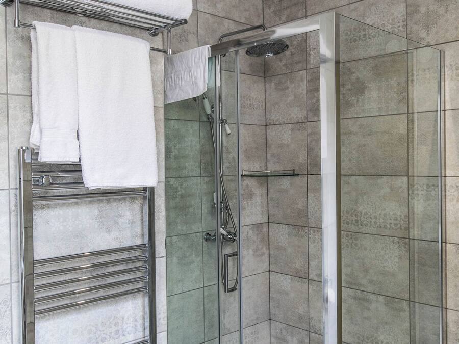 A modern bathroom with a glass-enclosed shower, a towel rack with folded towels, and a chrome towel warmer.