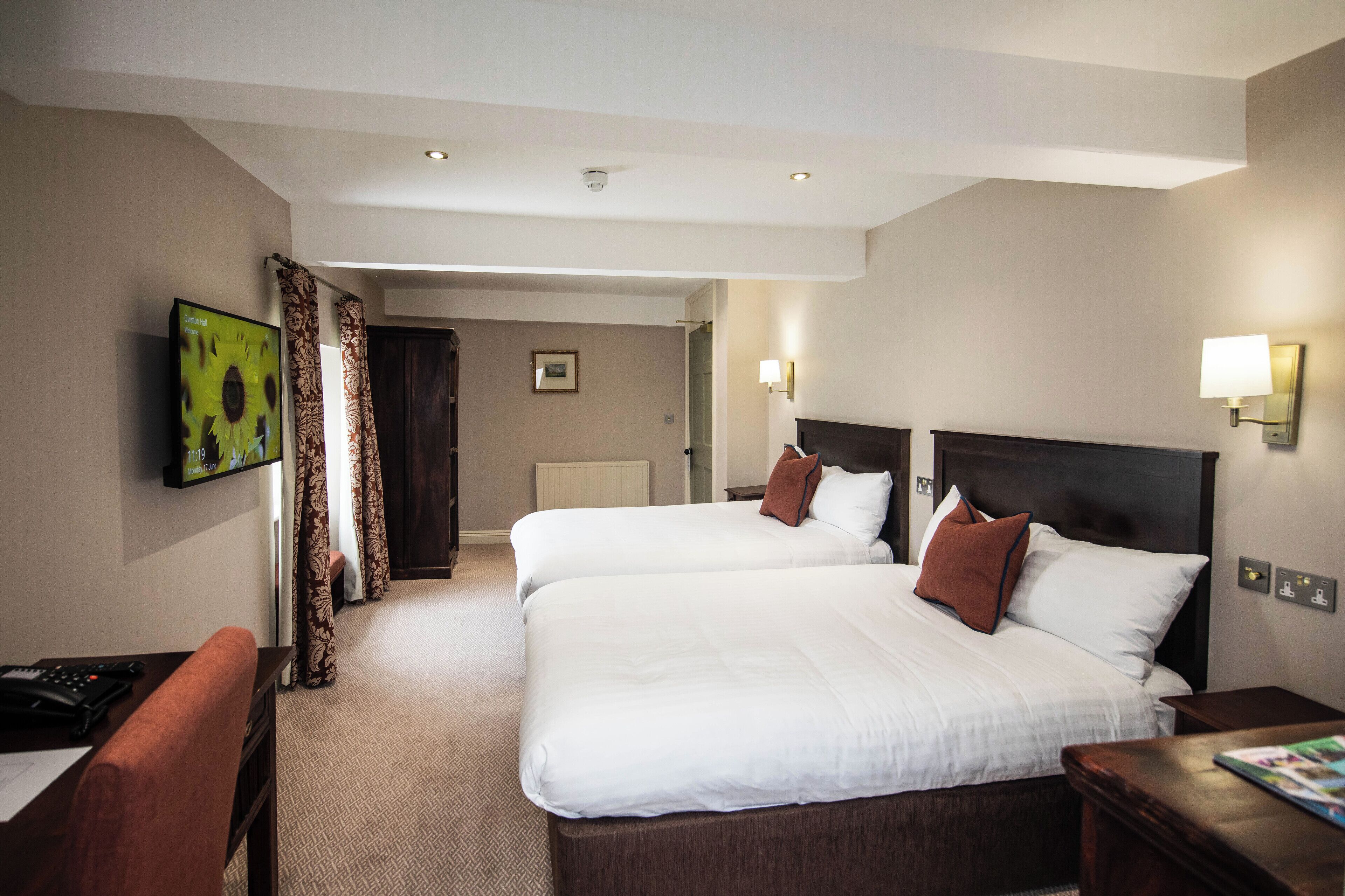 A hotel room with two beds, a desk, a TV, and a door leading to another room.