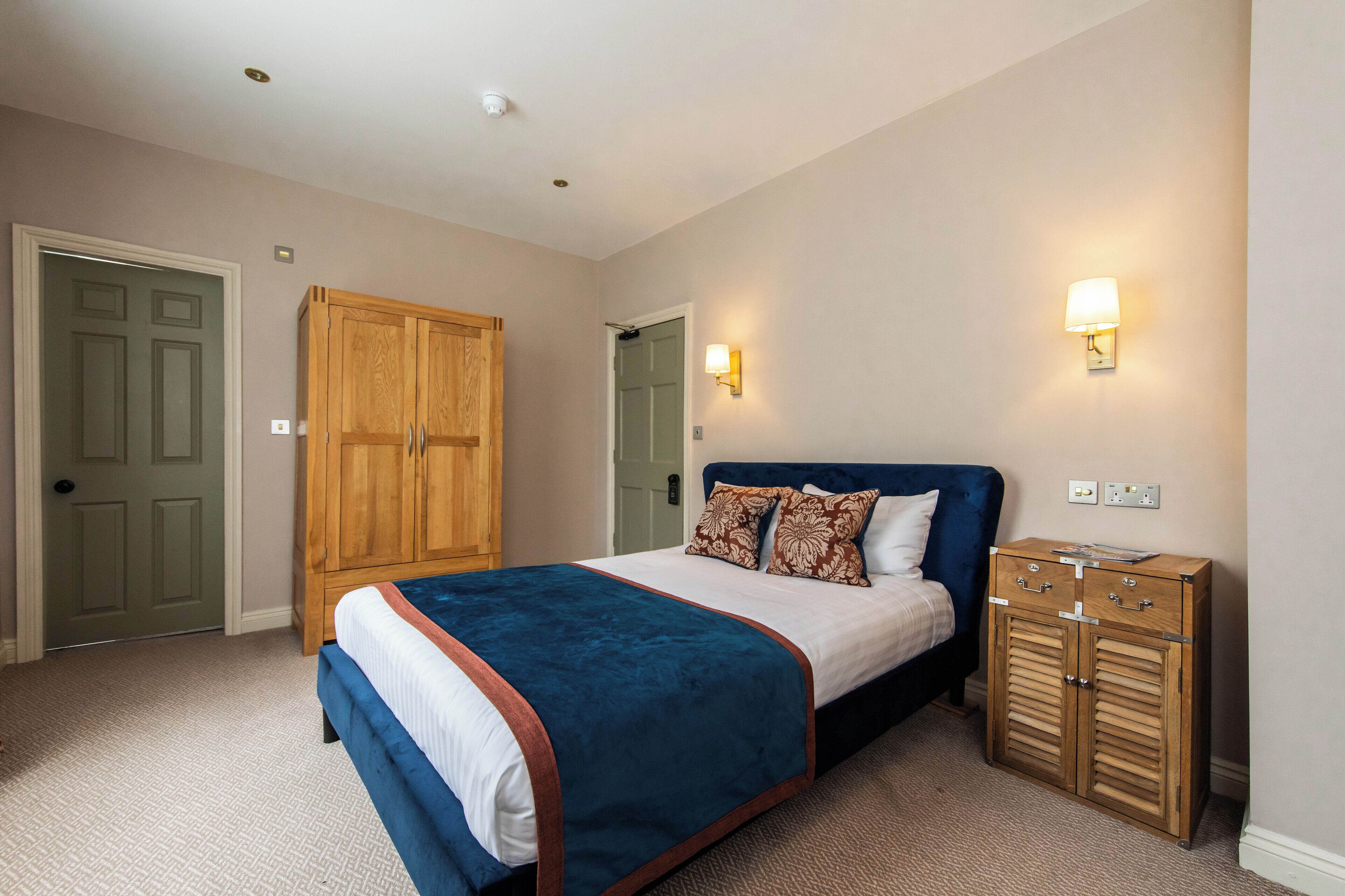 A bedroom with a bed, wooden wardrobe, and wall-mounted light fixtures.