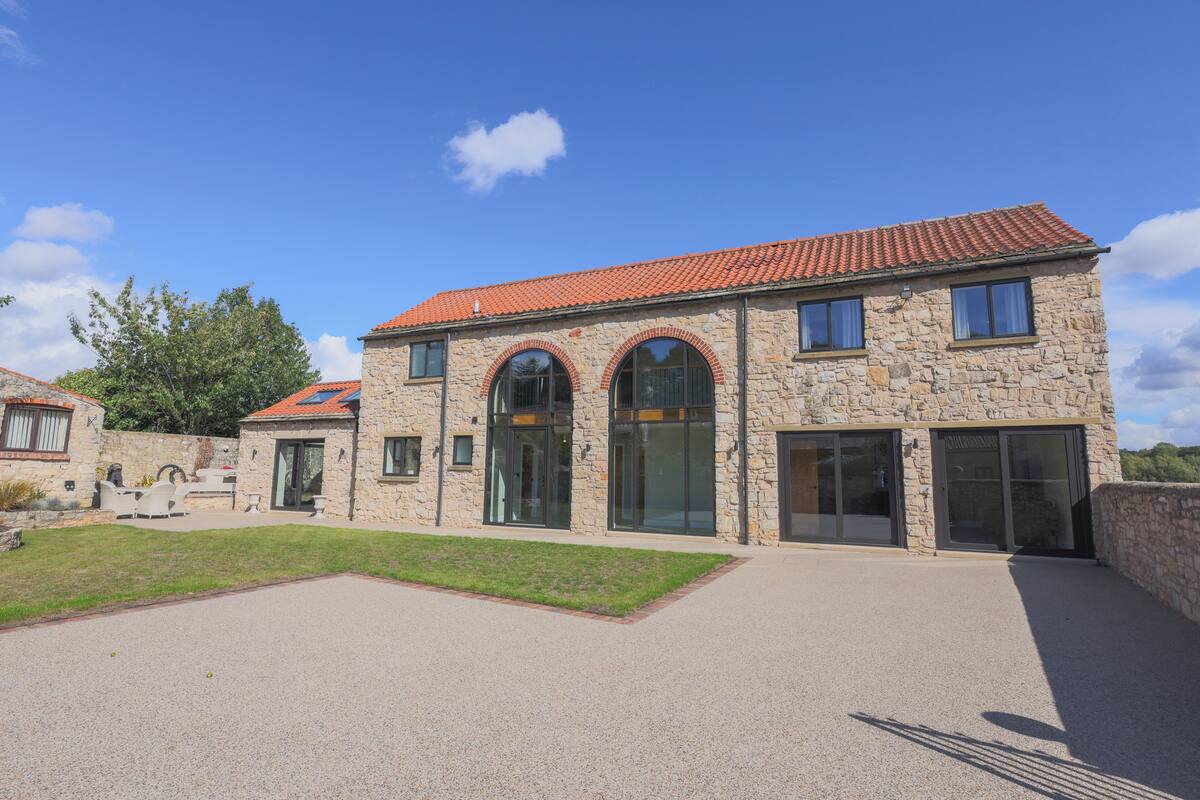 A stone building with a red-tiled roof, large arched windows, and a paved driveway.
