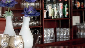 A bar area with shelves of liquor bottles and glasses, and two white vases with blue flowers. - Hotel Koogerend (Den Burg)