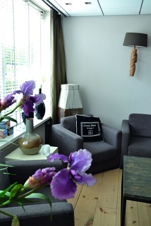 A modern living room with a sofa, a small table with a vase of flowers, and a lamp. - Hotel Koogerend (Den Burg)