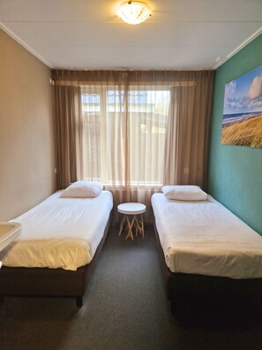 A hotel room with two single beds, a small round table, and a large window with curtains. - Hotel Koogerend (Den Burg)