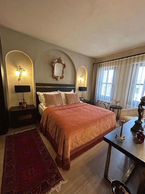 Habitación de hotel con una cama grande, dos lámparas de noche, un espejo, una mesita con una estatua y una alfombra roja.