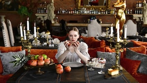 A woman sitting at a table with a fruit bowl, candles, and a statue. - Sacred Mansion (Nevsehir)