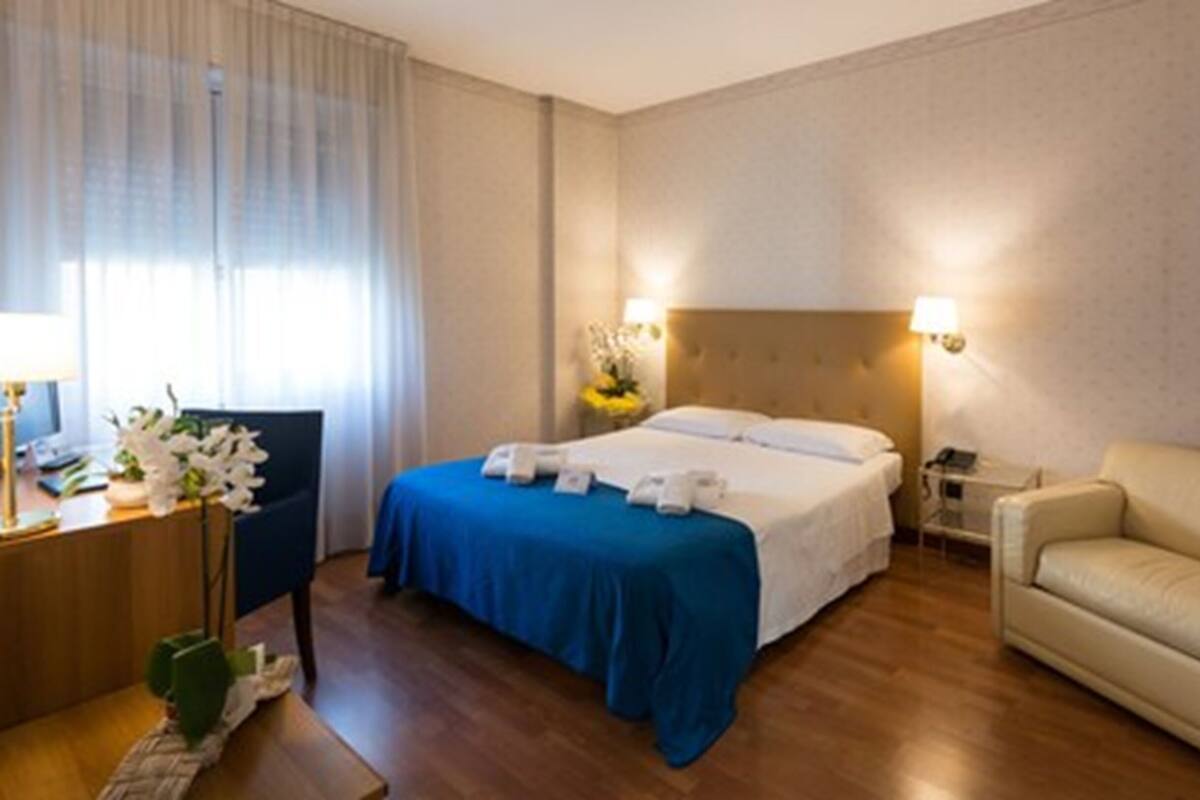 A hotel room with a bed, a desk with a lamp, a chair, and a sofa.