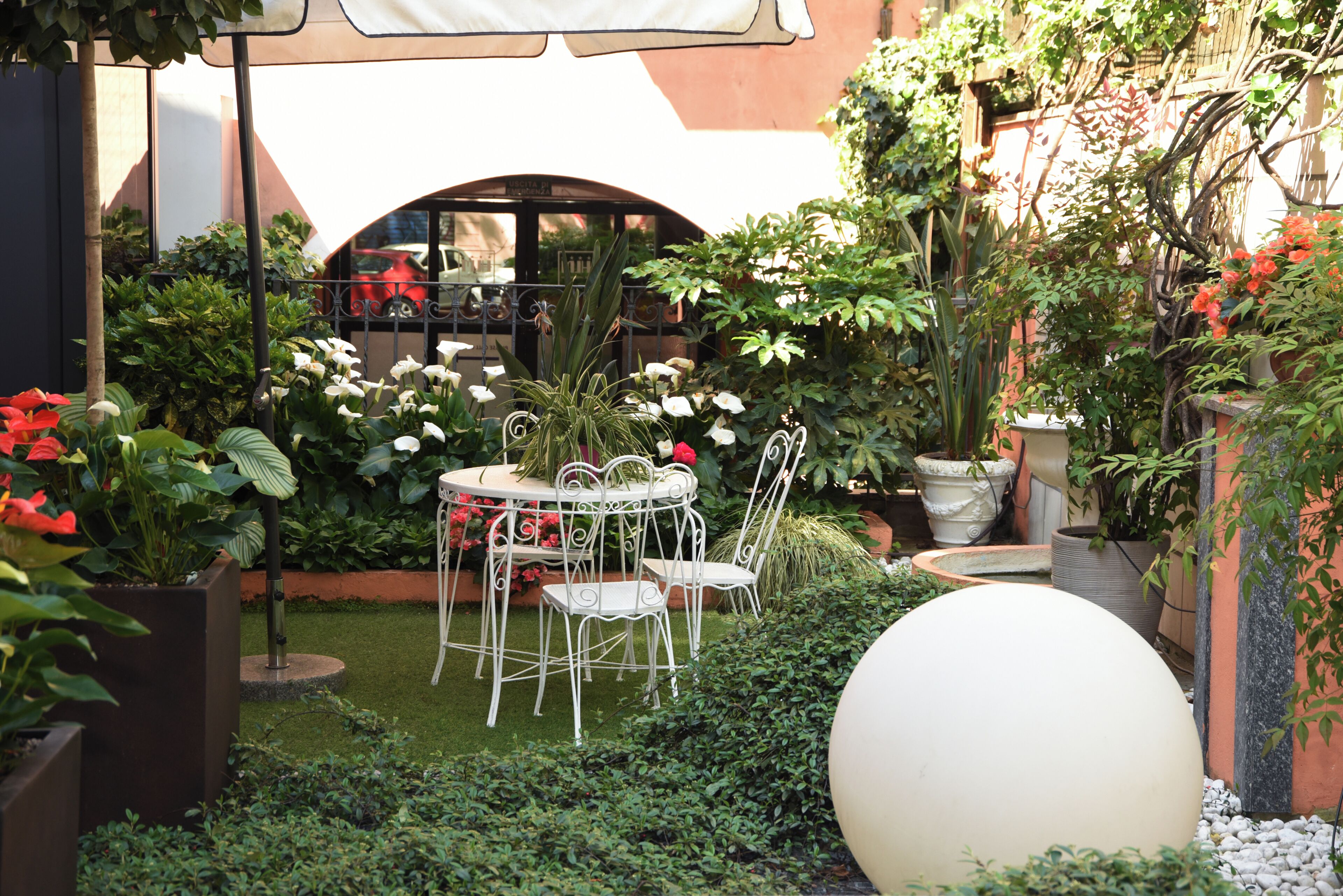 Een tuinpatio met een ronde tafel en stoelen, omringd door diverse planten en een grote bolvormige decoratie.