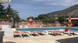 Area piscina con lettini e ombrelloni, cielo sereno e montagne sullo sfondo.