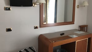 Camera d'albergo con un grande specchio, una televisione a schermo piatto, una toeletta in legno con specchio, due lampade a parete e un piccolo cestino.