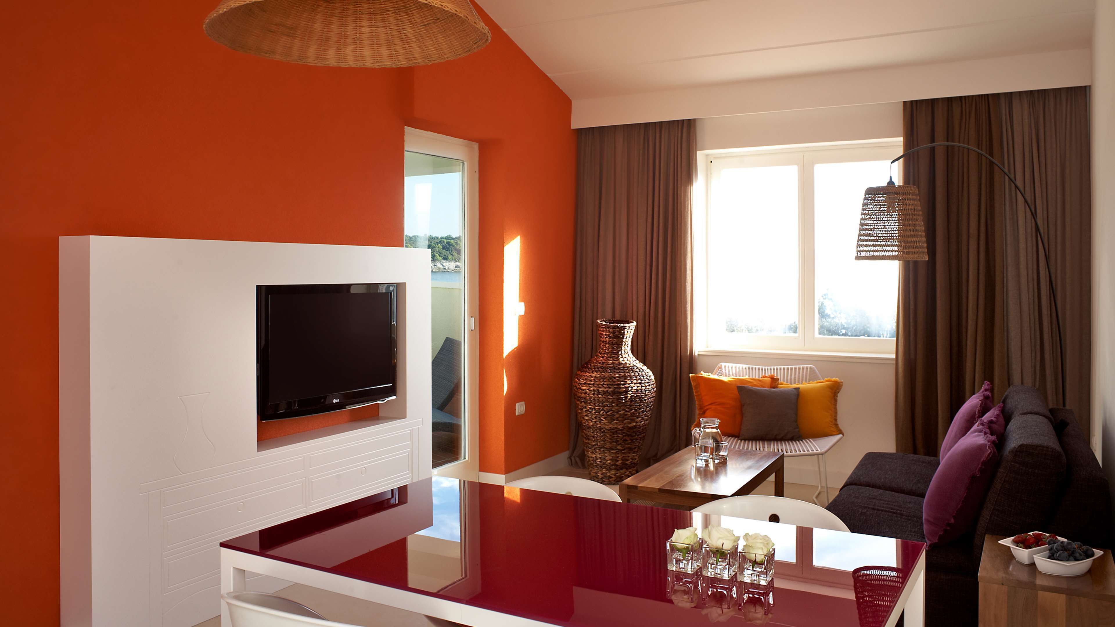Ein modernes Wohnzimmer mit Flachbildfernseher, einem Esstisch mit Stühlen, einer Vase und einer Couch mit Kissen.