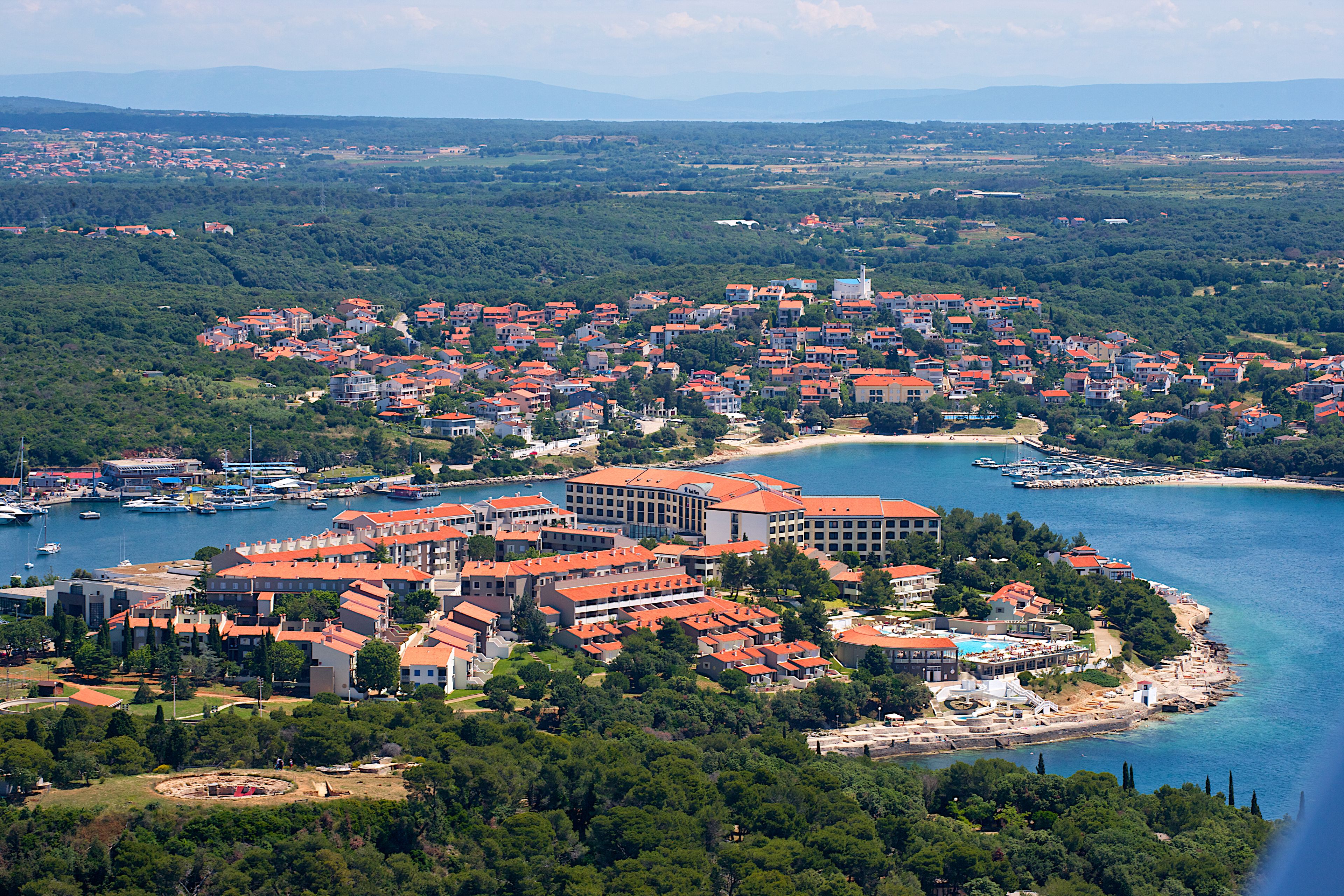 Une ville côtière avec des bâtiments aux toits rouges, un port de plaisance et une plage.