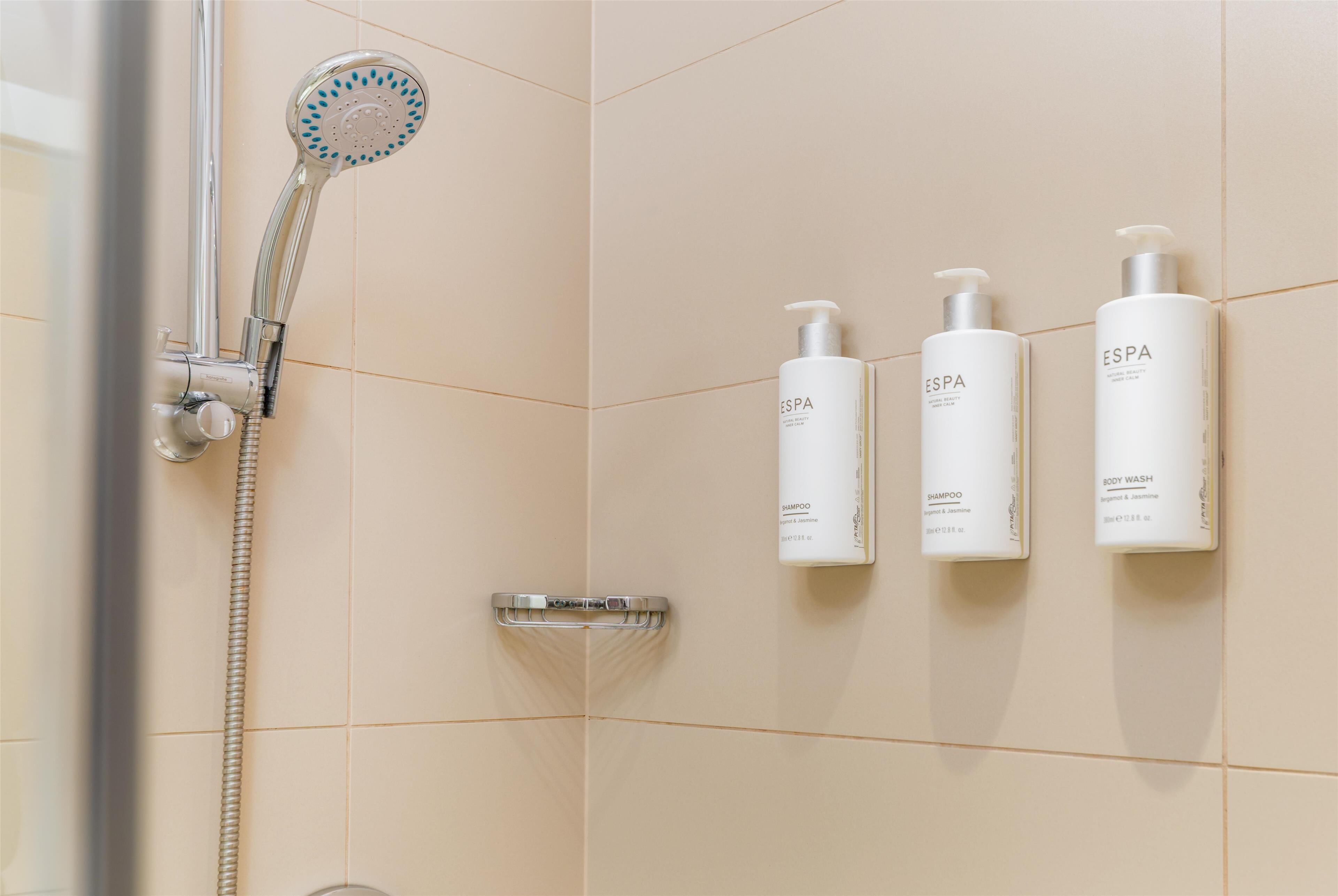 A bathroom with a shower, three bottles of ESPA body wash, and a handheld showerhead.