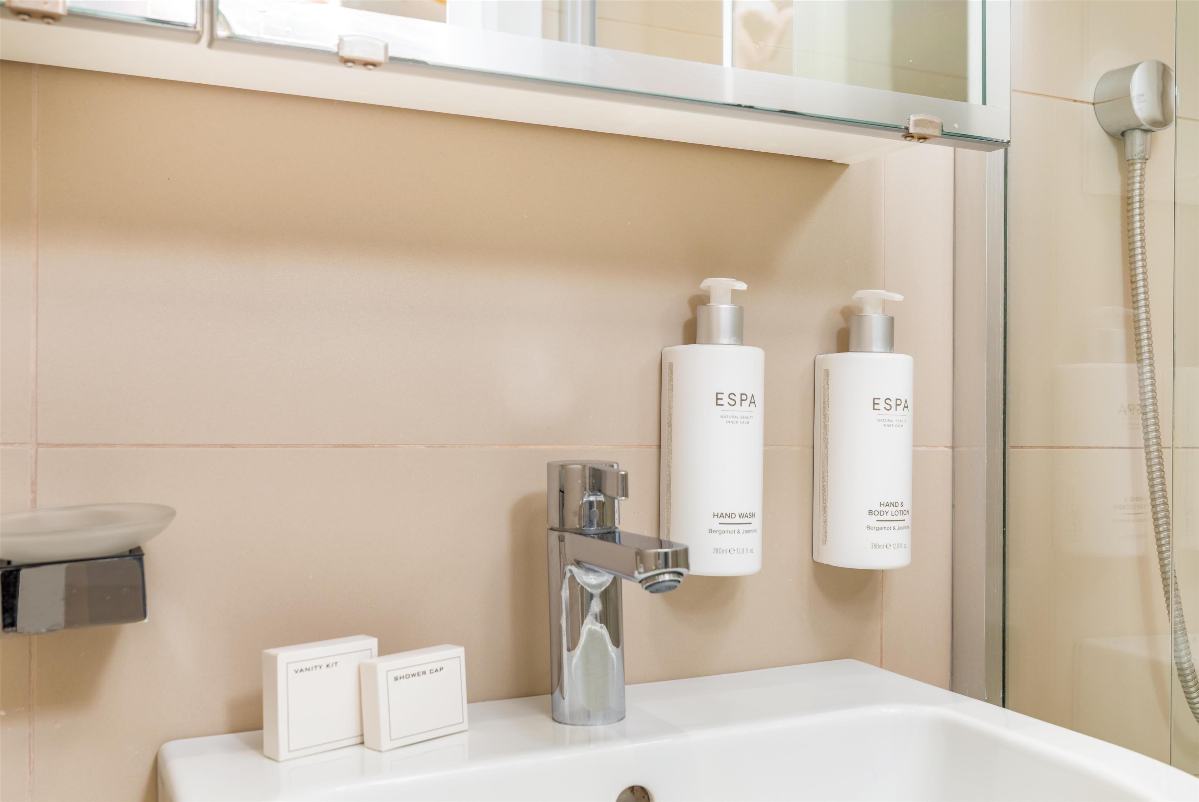 A modern bathroom with a glass shower enclosure, a white sink, and two hand soap dispensers labeled ESPA.