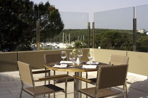 A round table with four wicker chairs, a vase with flowers, and wine glasses set for a meal. - Park Plaza Verudela Pula (Pula)