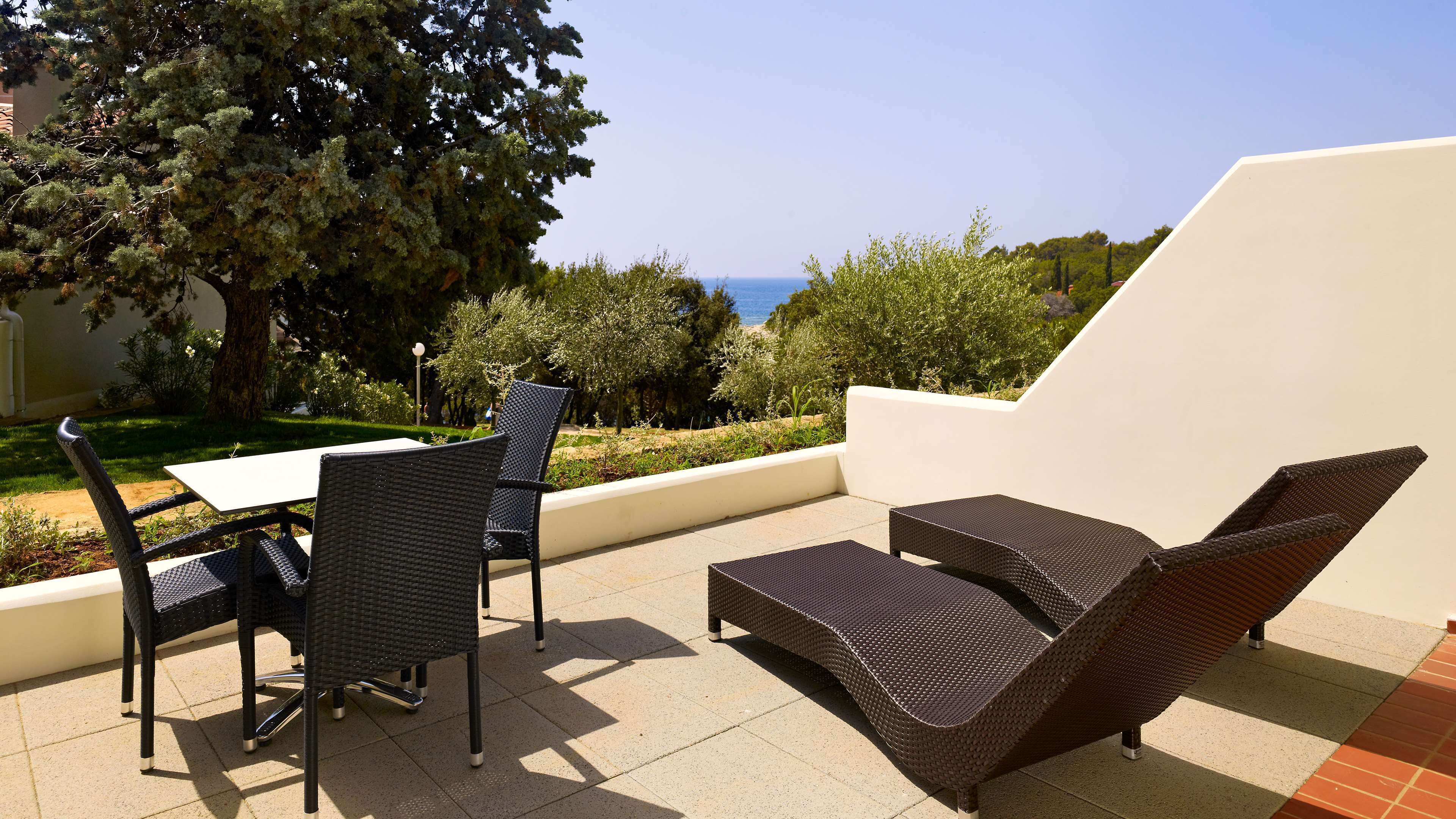 An outdoor patio with a table and chairs, a lounge area, and a view of the sea.