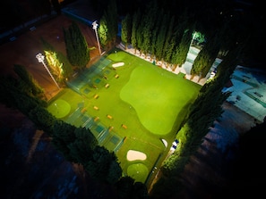 Ilmakuva golfkentästä yöllä, jossa valaistut alueet erottuvat, ja kentän ympärillä on puita ja aita.